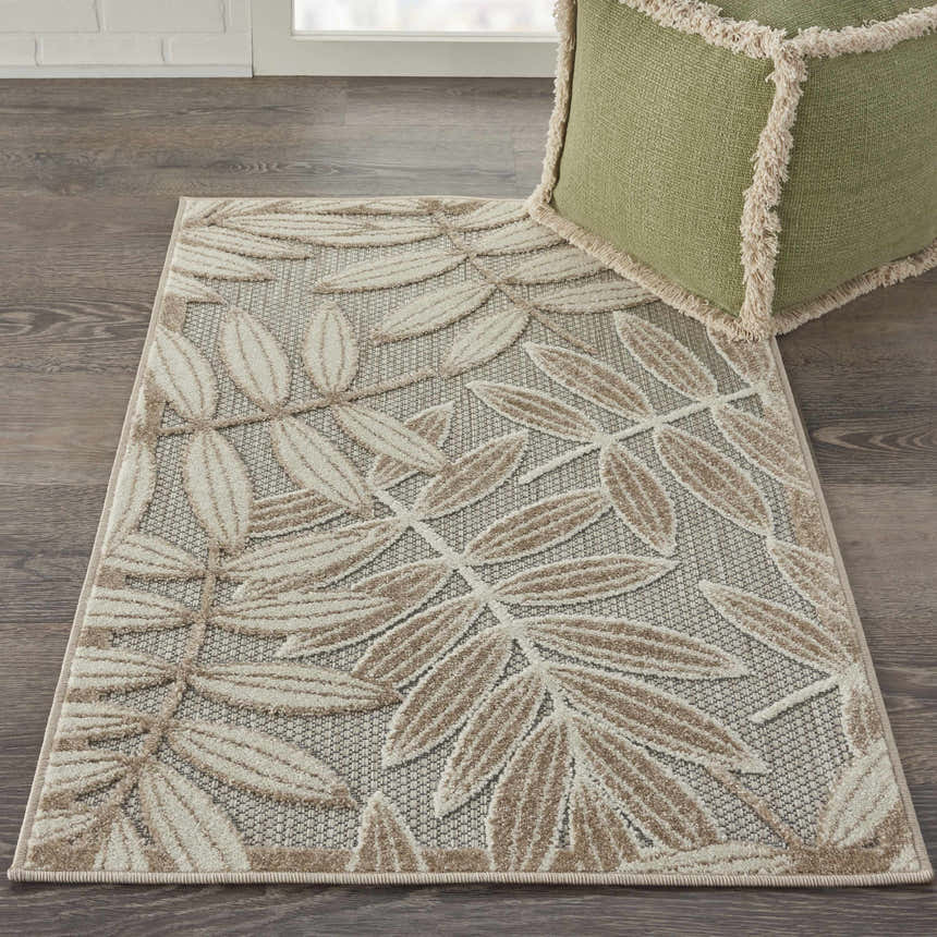 Close-up of the Nourison Aloha Natural Tropical Area Rug with a beige leaf pattern. Green fringed pouf.