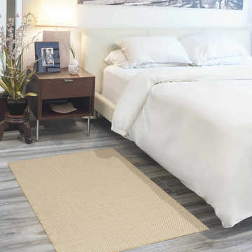 Bedroom scene with a Nourison Courtyard Natural rug, white bedding, wood nightstand, and gray wood-look floors.