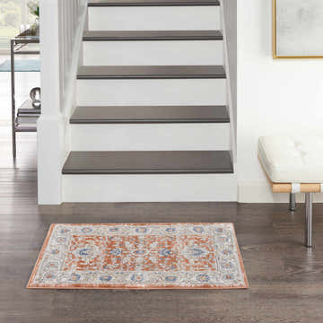 Entryway scene with Nicole Curtis Series 4 Grey Multicolor Vintage rug on dark wood floor near white stairs.