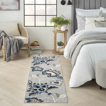 Bedroom scene with blue and gray Nourison Aloha outdoor runner rug, rattan chair, and light wood floors.