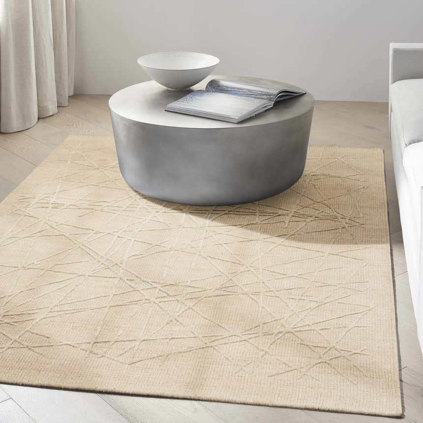 Minimalist living room with a Calvin Klein CK044 Wander Natural rug, round concrete table, and light wood floors.