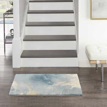Entryway with stairs and Nourison Prismatic Blue Multicolor rug. Modern home decor with wood floors and white bench.
