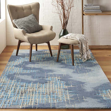 Living room scene with a blue beige Nourison Symmetry rug, mid-century chair, stool, and wood floors.