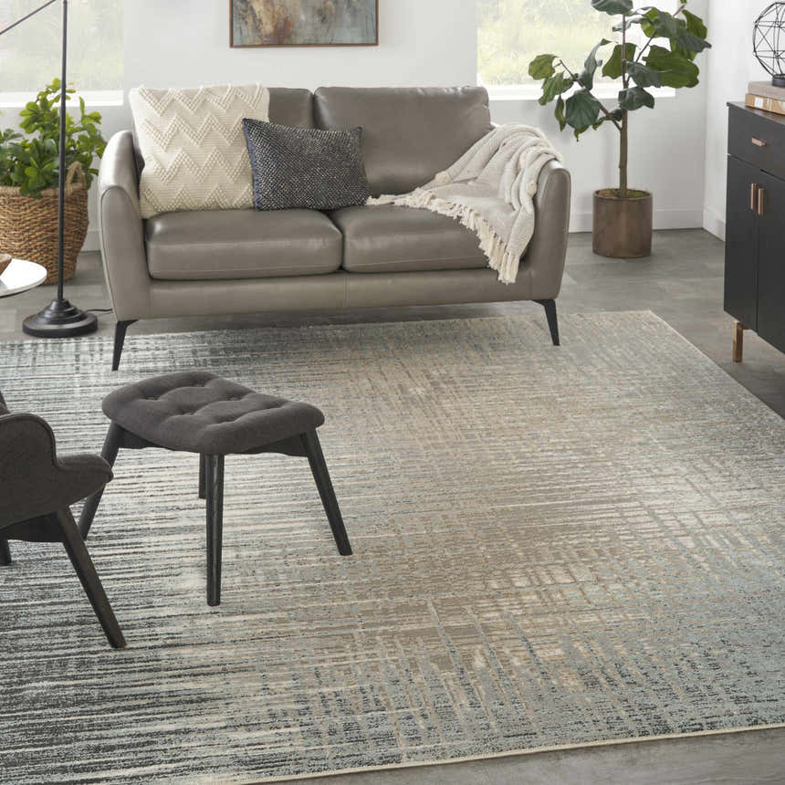 Living room scene with a Nourison Marmara Teal/Grey rug, grey sofa, ottoman, plants, and a modern, contemporary style.
