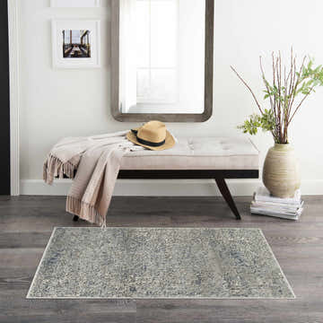 Entryway with a Nourison Quarry Dark Grey rug, bench with blanket, mirror, and wood floors.