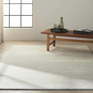 Minimalist room scene with a beige Calvin Klein Home Lunar rug, wood bench, and natural light.