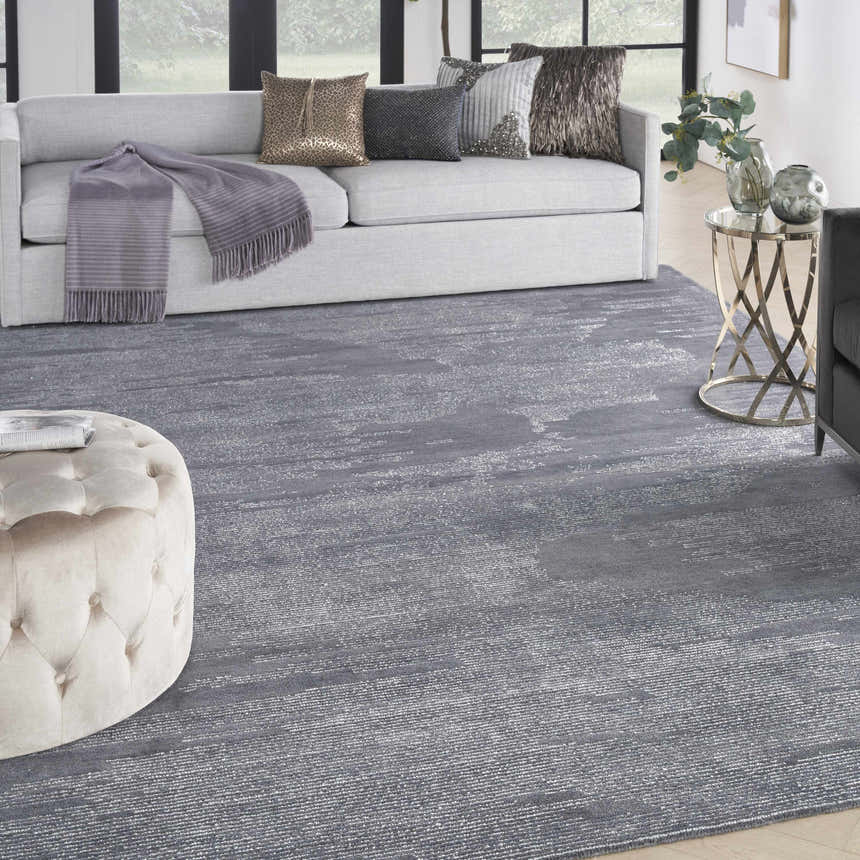 Living room scene with a gray Michael Amini Ma30 Star Blue rug, sofa, ottoman, and gold accent table.