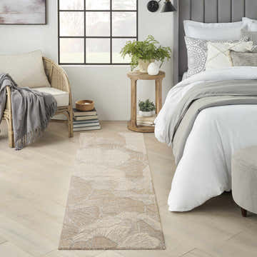 Bedroom scene with a Nourison Avra Taupe rug, rattan chair, and bed with white linens and gray accents.