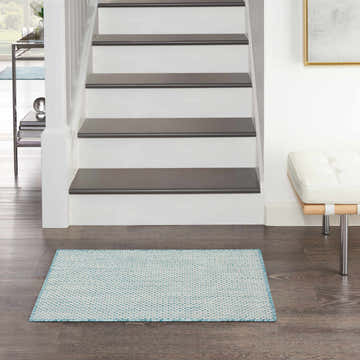 Entryway with Nourison Courtyard Ivory Aqua rug, dark wood floors, white stairs, and a modern white bench.