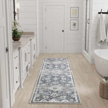 Bathroom scene with a Nourison Astra Denim Vintage rug runner on light wood floors. White cabinets and tub.