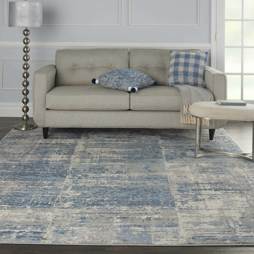 Living room scene with a Nourison Solace Ivory Grey Blue rug, light grey sofa, and blue accents.