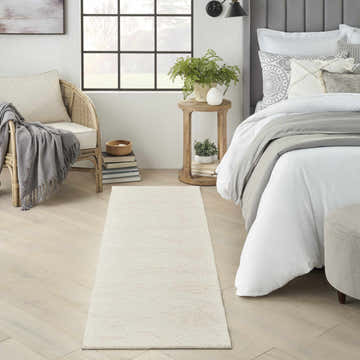 Bedroom scene with Nourison Avra Ivory rug, wood floors, rattan chair, and gray accents for a calm, modern look.