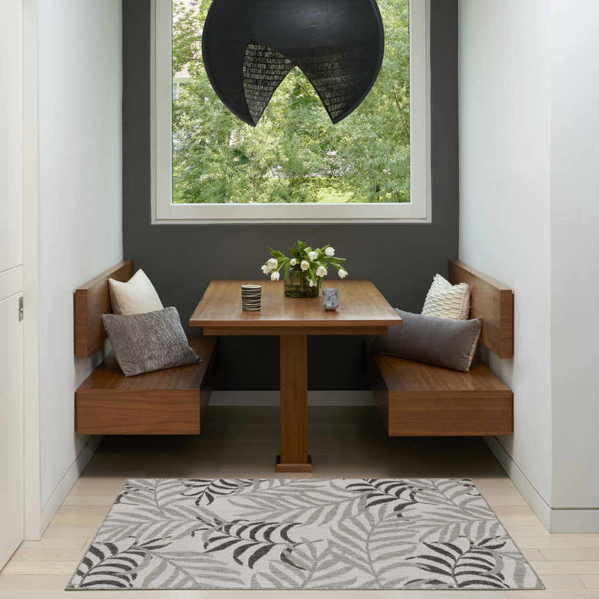 Breakfast nook with the Nourison Garden Oasis Grey Tropical Area Rug, wood benches, and a view to the garden.