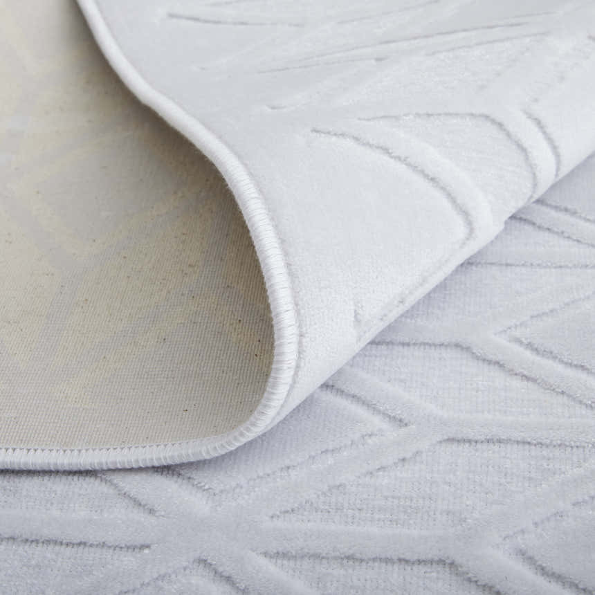 Close-up of Feizy Saphir Mira white area rug showing geometric swirls, soft texture and backing. Fold