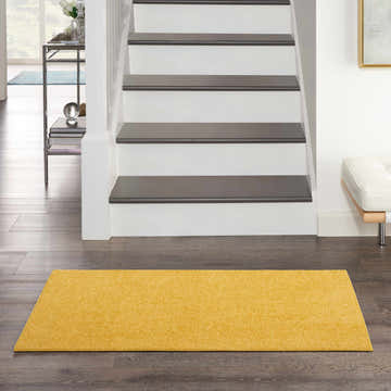 Hallway scene with a Nourison Essentials Yellow Outdoor Area Rug on dark wood floors near stairs.