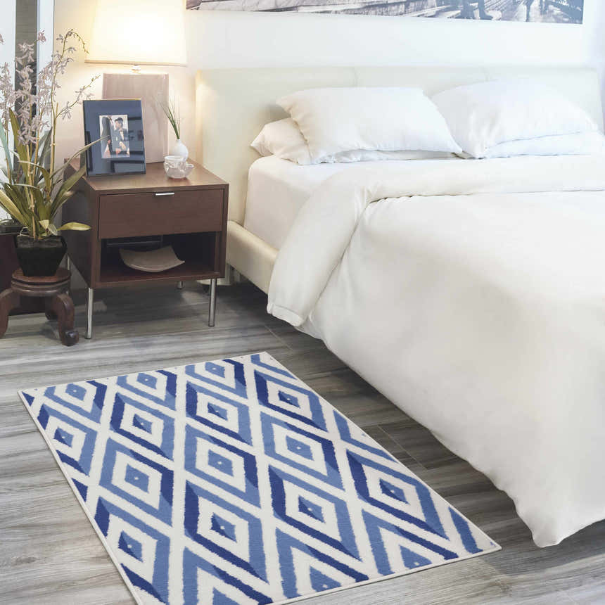 Modern bedroom scene with a Nourison Whimsicle Ivory Blue rug, white bedding, and a wood nightstand.