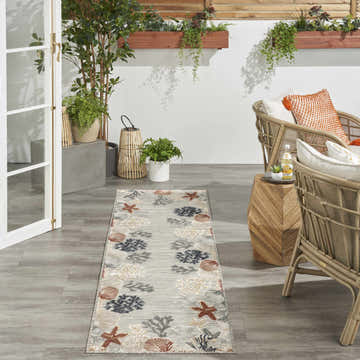Coastal patio with wicker chairs and Nourison Suncoast grey multicolor rug featuring starfish and seashell pattern.