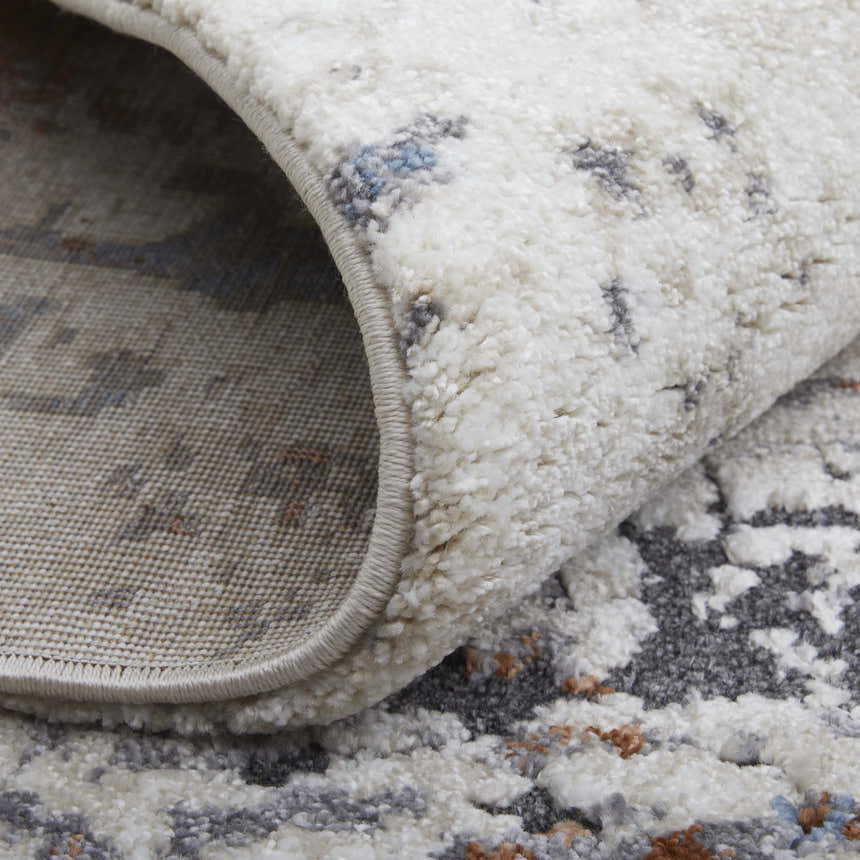 Close-up of Feizy Gilmore rug texture. Ivory rug with abstract blue and gray pattern, shows rug backing. Fold