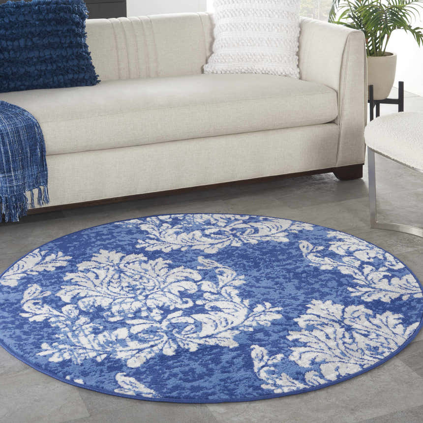 Living room scene with a round Nourison Whimsicle Navy Ivory rug, beige sofa, blue throw, and plant. Farmhouse style.