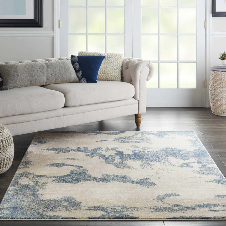 Living room scene with a Nourison Etchings Ivory/Light Blue rug, cream sofa, and dark wood floors. Modern style.