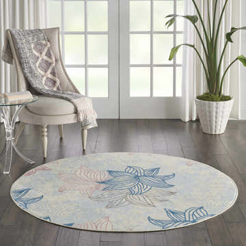 Sunlit room with Nourison Jubilant Ivory Multicolor rug, floral design, round shape. Chair, plant, and dark wood floors.
