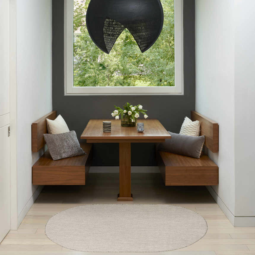 Breakfast nook with wood benches, table, and round Nourison Courtyard Ivory Silver Modern Area Rug on light wood floors.