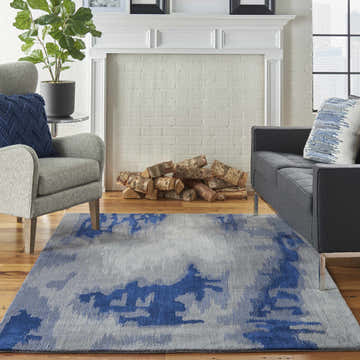 Living room scene with Nourison Symmetry Grey Blue rug, gray sofa and armchair, and white fireplace.