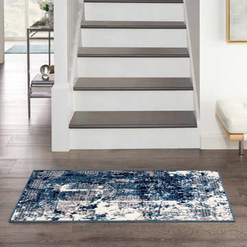 Entryway with Nourison Grafix Navy Blue rug, dark wood floors, white stairs, and modern decor.