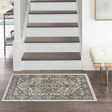 Entryway scene with Nourison Quarry Ivory Blue vintage rug, dark wood floors, white stairs, and modern white bench.