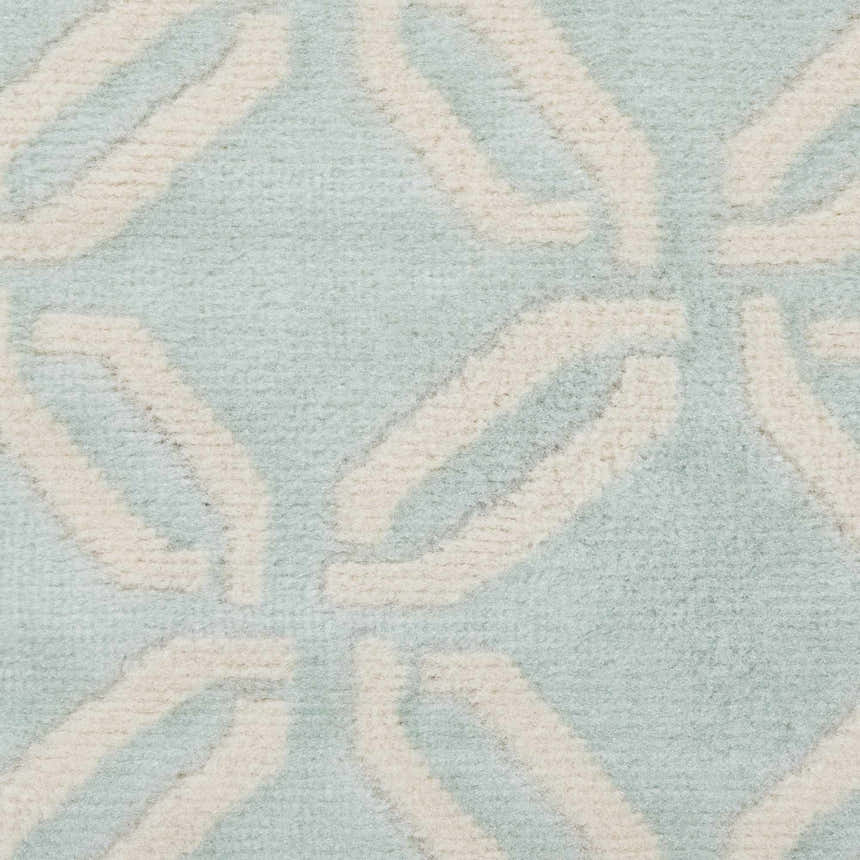 Close-up of the Nourison Jubilant Green rug showing a geometric, interlocking ivory pattern on a light green background.