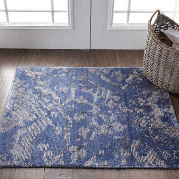 Entryway with Nourison Lucent Dusk vintage rug in blue and beige, wood floors, white door, and woven basket.