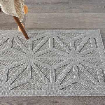 Close up of Nourison Cozumel Light Grey rug with geometric pattern on gray wood floor, styled with chair.