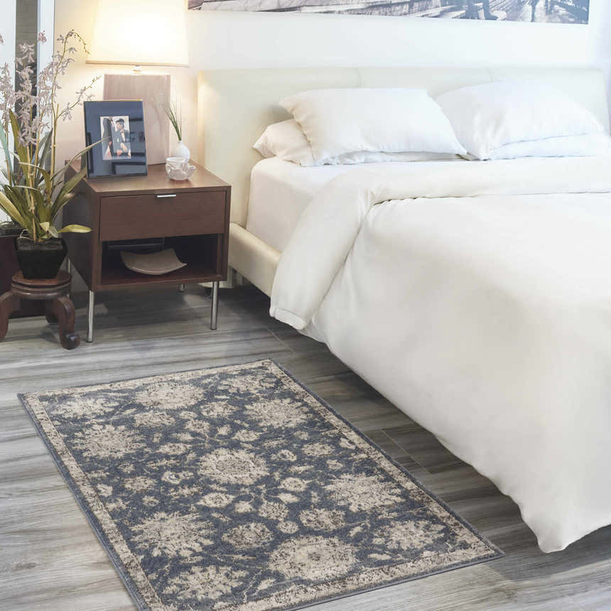 Bedroom scene with a Nourison Quarry Blue Beige vintage rug on gray wood floors. White bedding and wood nightstand.