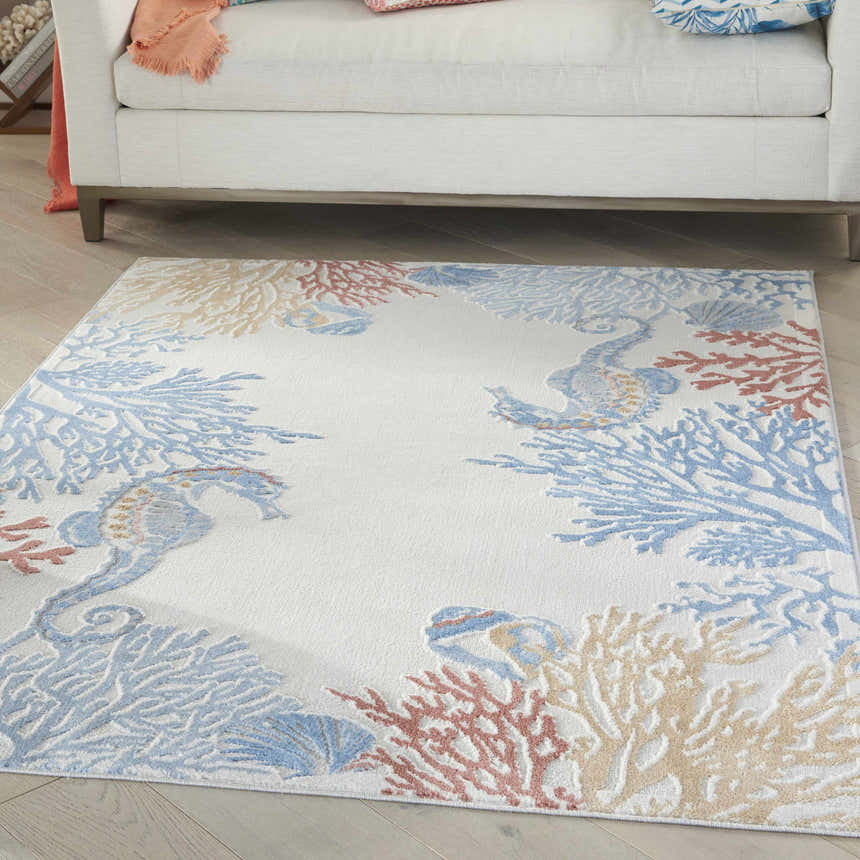 Living room scene with a Nourison Seaside Ivory rug featuring coral and seahorse design under a white sofa.