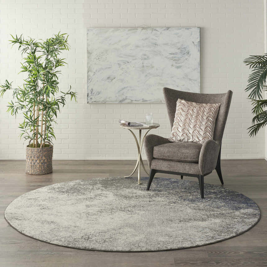 Living room scene with a round Nourison Passion Charcoal Ivory rug, gray chair, and white brick wall.