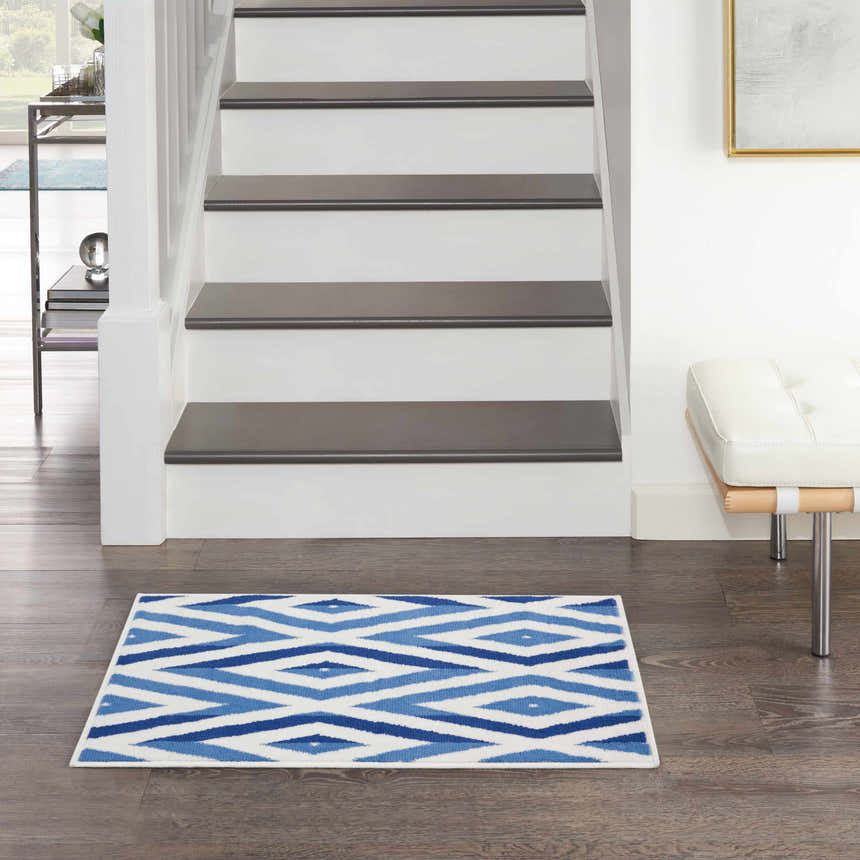 Entryway scene with Nourison Whimsicle Ivory Blue rug, wood floors, white stairs, and a modern white bench.
