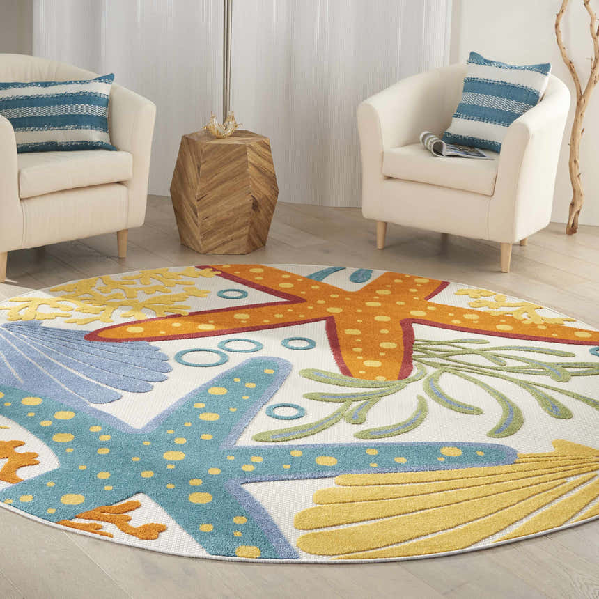 Coastal living room with white chairs and a round Nourison Aloha Multicolor area rug featuring starfish and seashell designs.