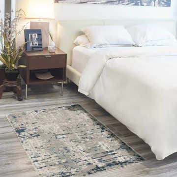 Modern bedroom scene with a Nourison Quarry Ivory Grey Blue area rug on wood floor next to white bed.
