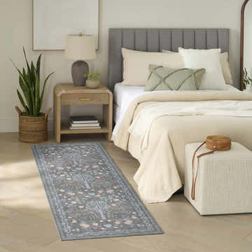Bedroom scene with Nourison Botanical Charcoal Multicolor rug, wood floors, neutral bedding, and a light wood nightstand.