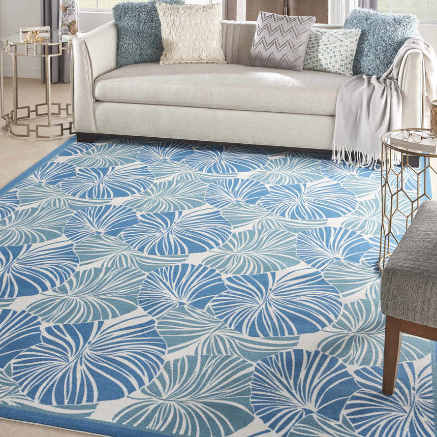 Living room scene with a Waverly Sun N' Shade Blue Tropical Area Rug, light sofa, and blue throw pillows.