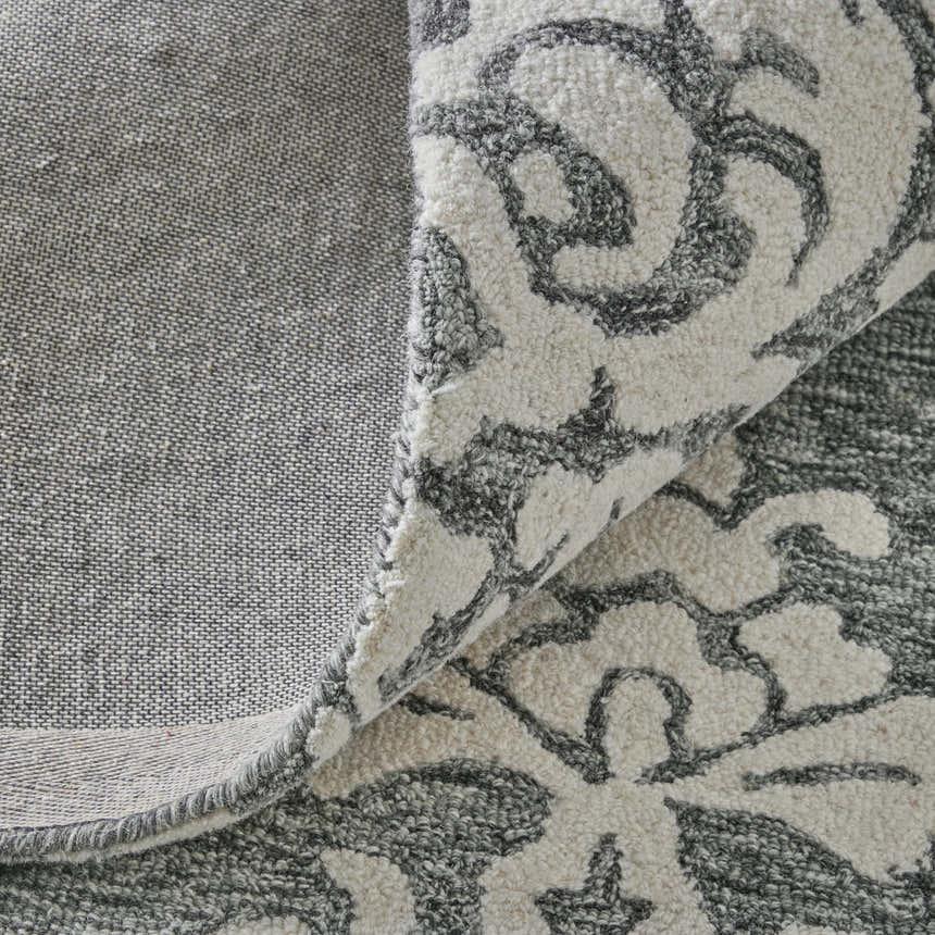 Close-up of the Feizy Belfort rug showing gray floral pattern on ivory wool, and the rug's backing. Fold