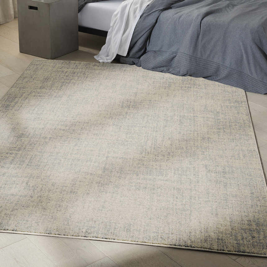 Bedroom scene with Calvin Klein CK030 Currents Beige Grey Rug, wood floors, gray bedding, and concrete side table.
