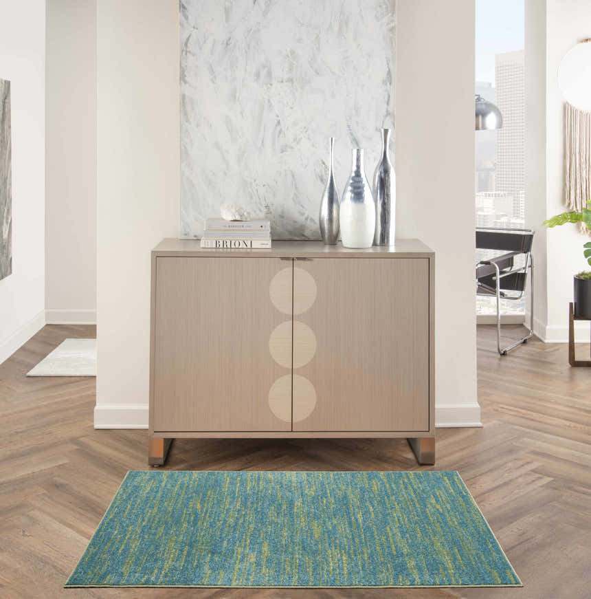 Living room scene with a Nourison Essentials Blue Green Outdoor Area Rug, cabinet, and herringbone wood floors.