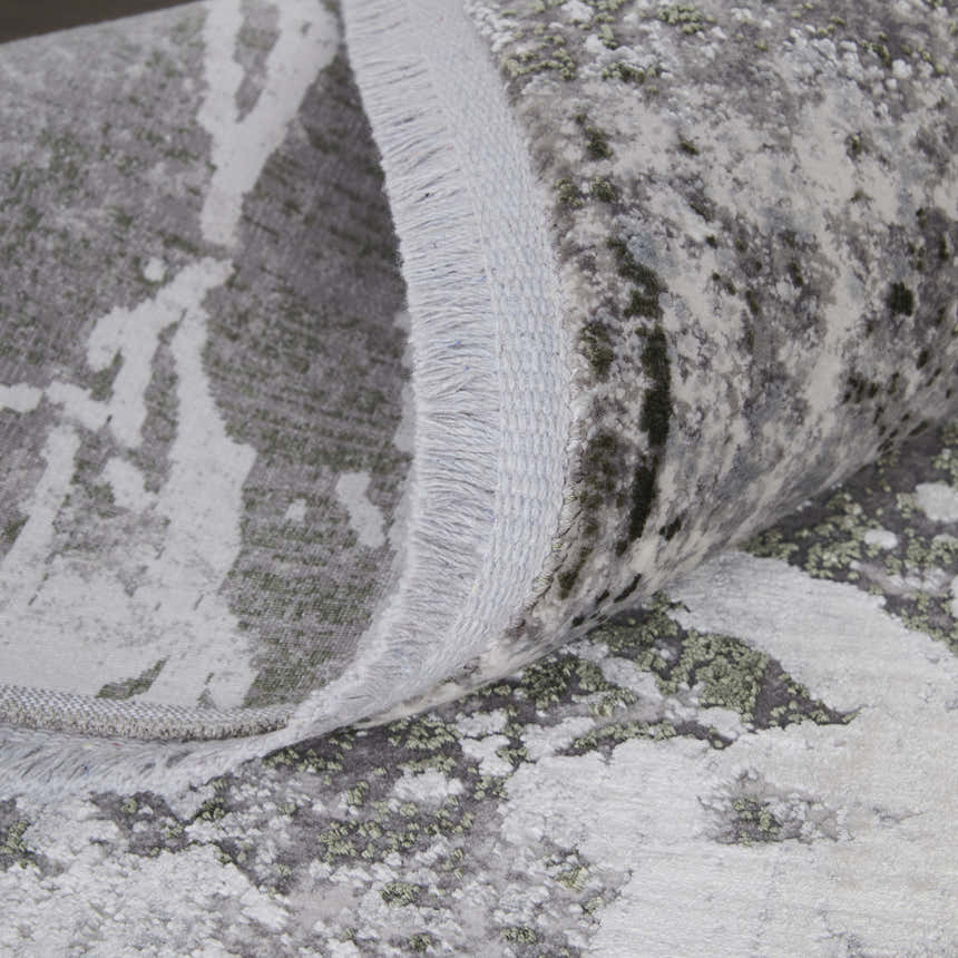 Close-up of the Feizy Cadiz rug showing its gray, green, and taupe abstract pattern and fringed edge. Fold
