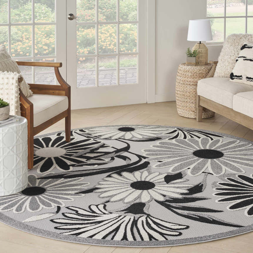 Sunroom with a round Nourison Aloha Black White Outdoor Area Rug, sofa, and wood chair.