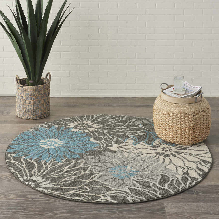 Round Nourison Passion Charcoal Blue rug with floral design in a styled room with plant and woven ottoman.