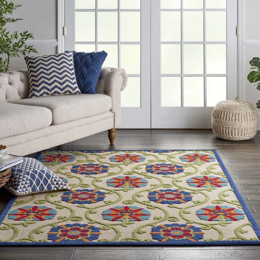 Living room scene with a Nourison Aloha Blue Multicolor rug, beige sofa, blue pillows, and a woven ottoman.