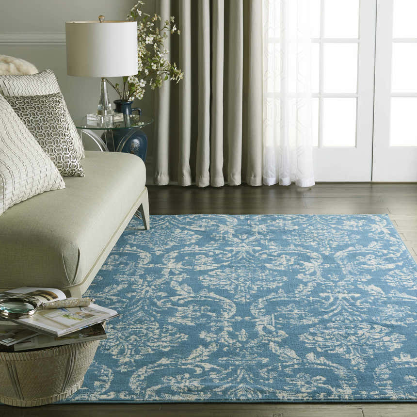 Living room scene with a light blue Nourison Jubilant Vintage rug, sofa, white curtains, and dark wood floors.
