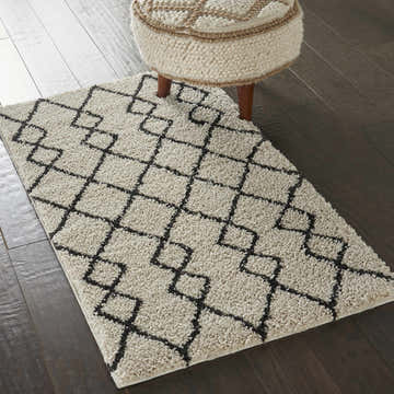 Close-up of the Nourison Martil Ivory/Charcoal Moroccan shag rug with geometric pattern on dark wood floors with a cream ottoman.