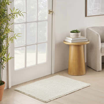 Entryway scene with a DKNY Pure Knots Ivory rug, light wood floors, white door, and bamboo plant.